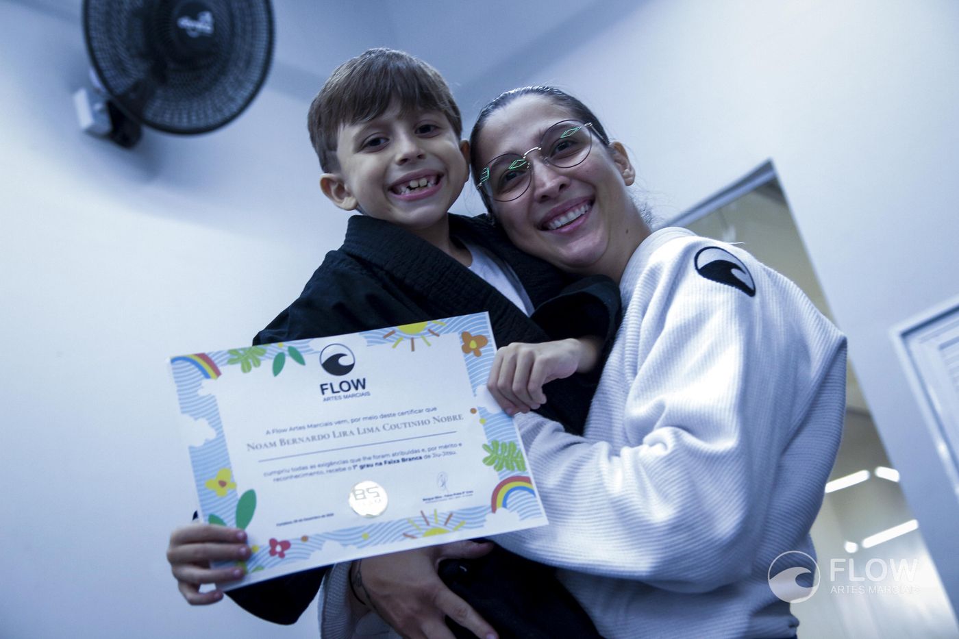 Aluno mostrando o certificado de graduacao ao lado da professora na Flow Artes Marciais